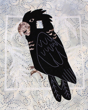 Black Cockatoo quilt pattern features a black parrot with gray beak and feet on a white square of jungle leaves stitched on a gray spotted fabric.  Buy at Raspberry Lane Crafts.  Black and White Birds Collection.